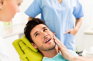 Man With Hand On Mouth In Dentist Chair, Mouth Open and Looks To Be In Pain