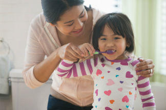 Mother helping daughter brush teeth